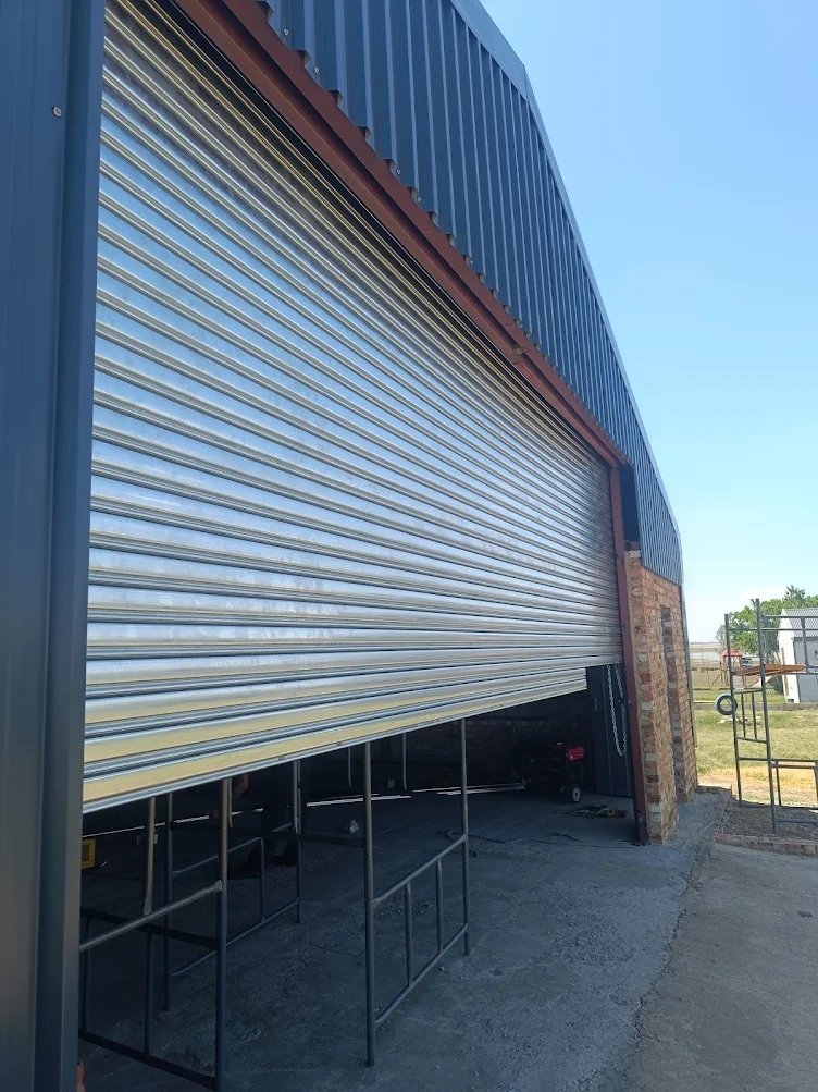 Large silver industrial roller shutter door partially open on steel structure